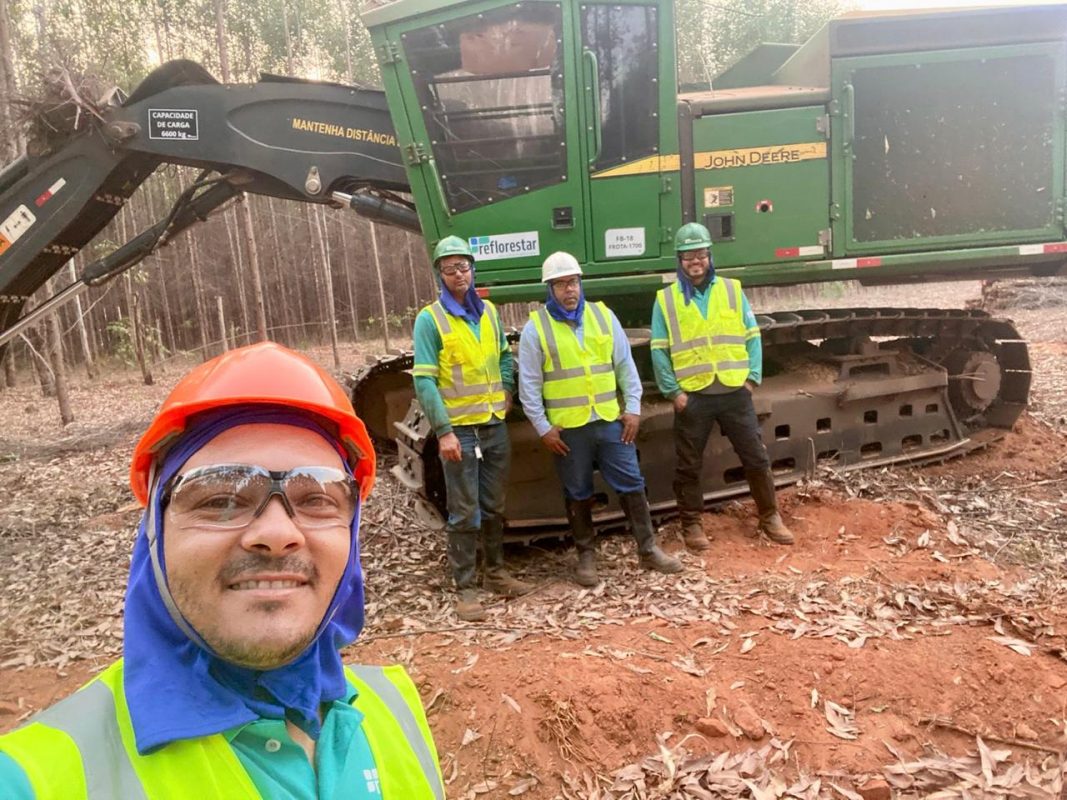 4 Trabalhadores área de plantio com um trator atrás.